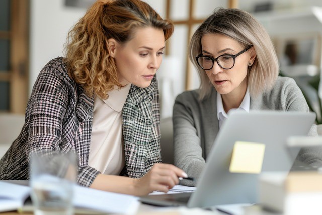 Two ladies in business dress looking at a laptop